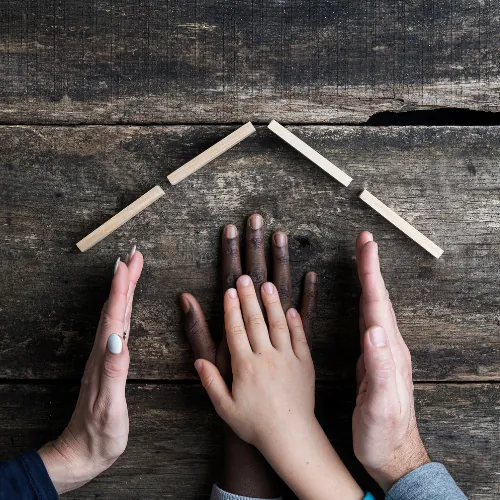 Hands of different skin tones gathered under a roof shape made of wooden sticks